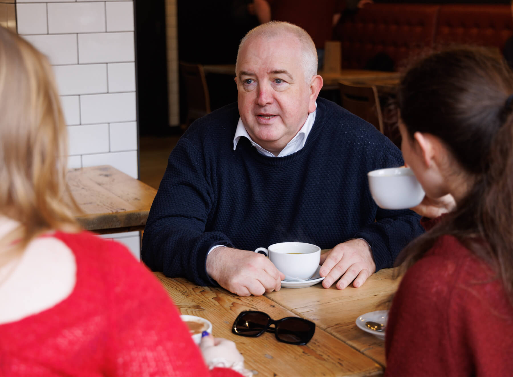 three people sitting down at a table drinking from white cups